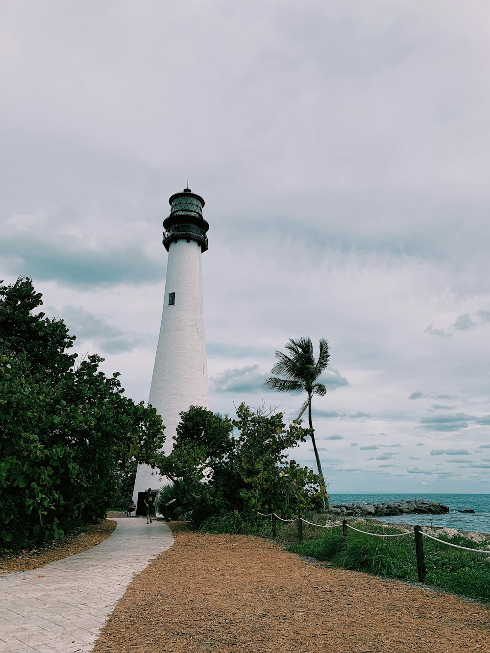 white and black lighthouse near green trees under white clouds during daytime