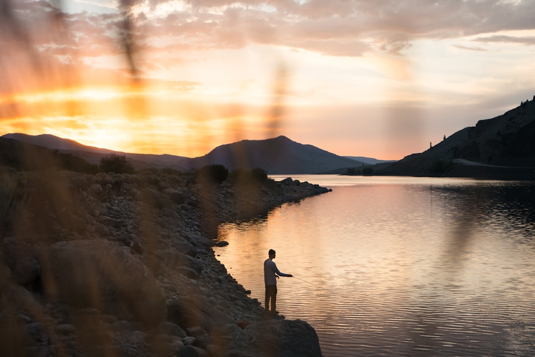 person standing on rock near body of water during sunset