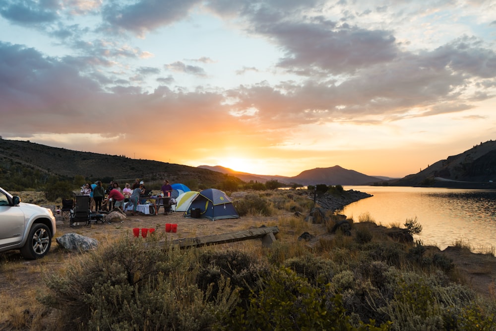 people sitting on camping tent near lake during sunset