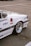The image captures a close-up view of a white sports car parked on an asphalt surface. The car features various decals and logos such as Nissan PDC, FET Kyokuto, SSR, and HKS. The focus is on the rear section of the car, showcasing the distinctive rims and the sleek bodywork.