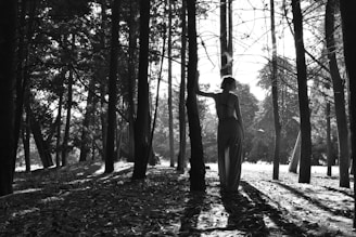 A woman holding a shamanic drum in a forest clearing with sunlight filtering through the trees.