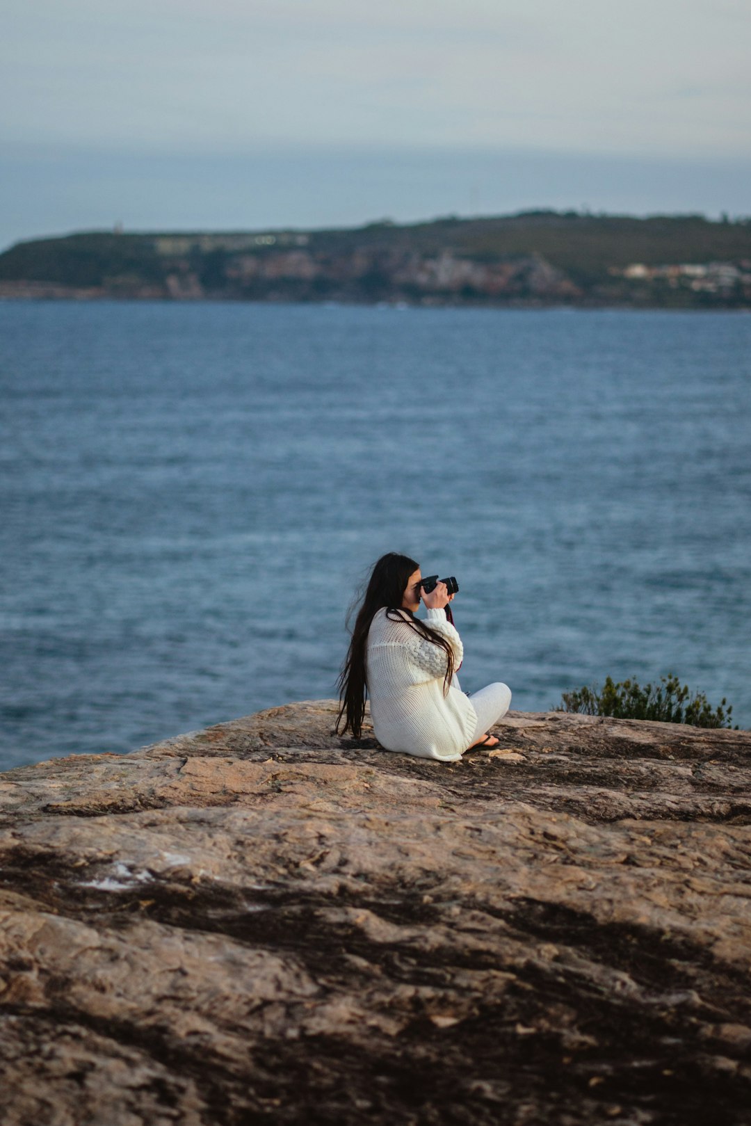 woman in white dress sitting on rock by the sea during daytime