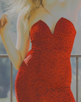 A person is wearing a strapless, floral-patterned dress in vibrant red. The dress has a form-fitting design and intricate lace details. The person's hair is flowing down and illuminated by sunlight, contributing to the bright and vivid atmosphere.
