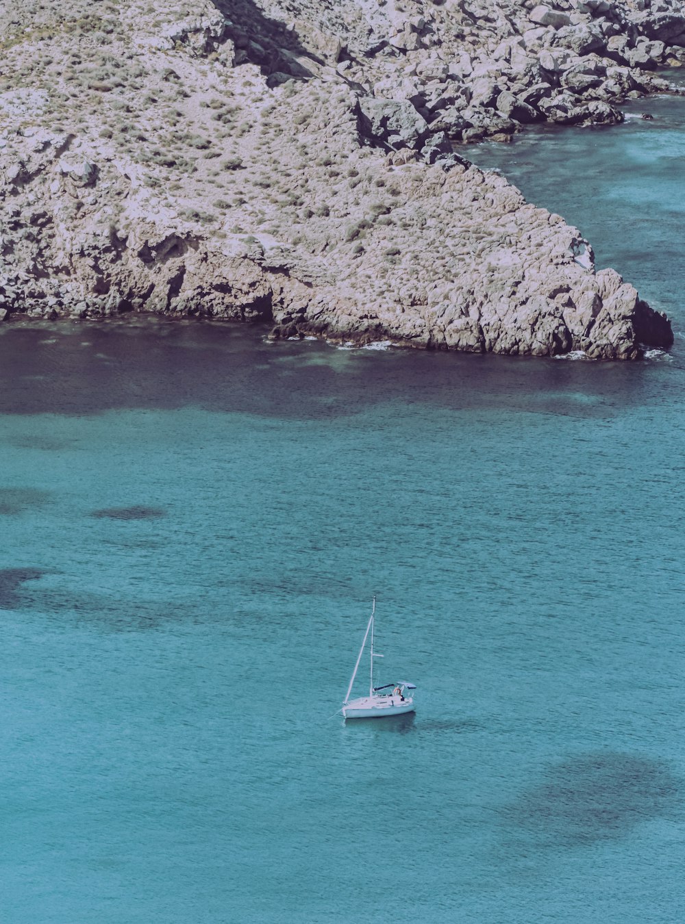 Barco blanco en el mar azul junto a la montaña rocosa marrón durante el día