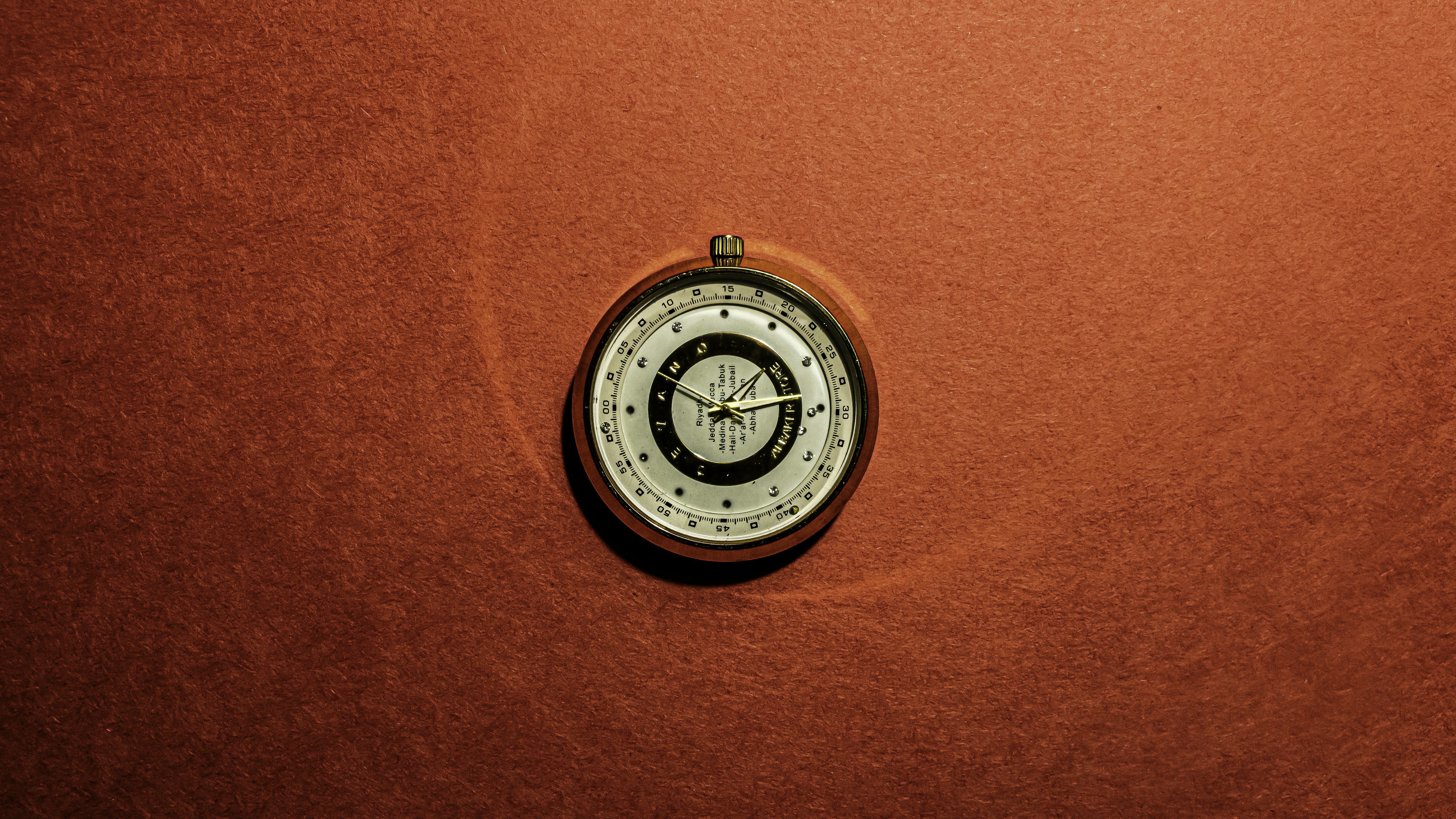 A vintage-style compass is placed on a textured brown surface. The compass features a metallic finish with intricate markings and a needle pointing in a specific direction.
