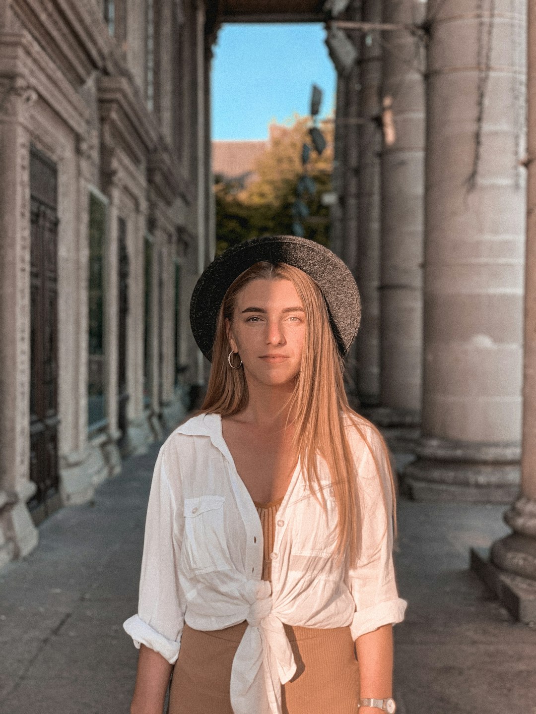 woman in white dress shirt and black hat standing near building during daytime