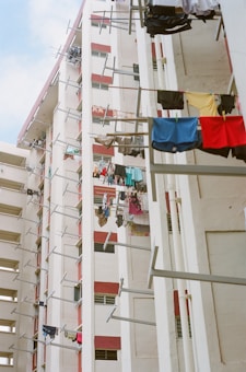 High-rise residential buildings featuring laundry hanging on poles extended from the windows. The walls of the buildings are painted in a mix of white and red. The image conveys a sense of urban living and community.