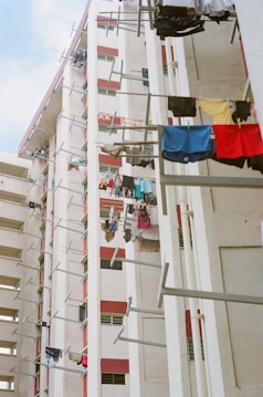 High-rise residential buildings featuring laundry hanging on poles extended from the windows. The walls of the buildings are painted in a mix of white and red. The image conveys a sense of urban living and community.