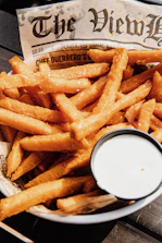 Basket of golden fries with a side of dipping sauce on a bright table.