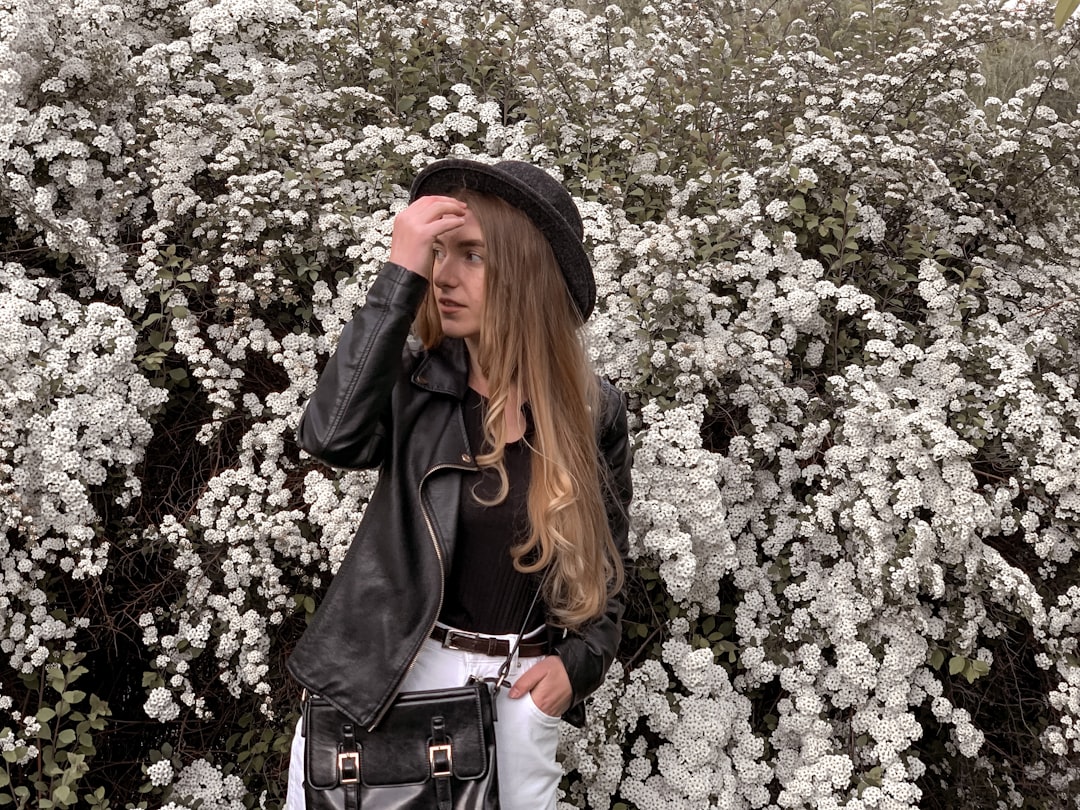 woman in black leather jacket standing near white flowers
