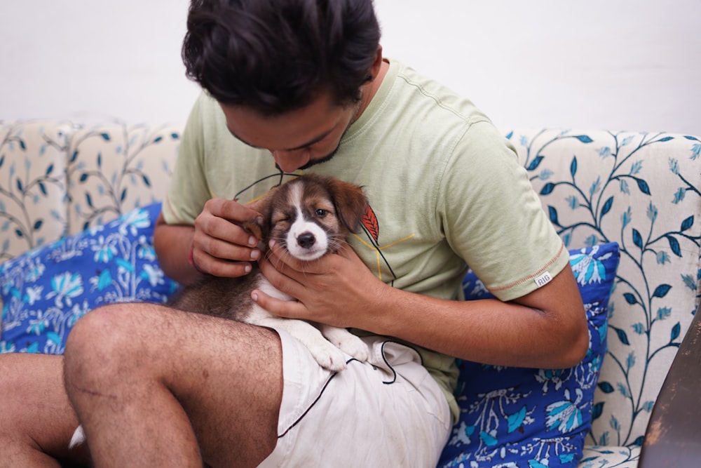 homem na camiseta verde do pescoço da tripulação segurando o filhote de cachorro marrom e branco