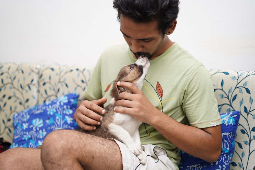 man in green crew neck t-shirt holding brown and white puppy