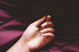 Softly lit hand with glossy deep red nails resting on a cream silk fabric.