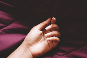 Softly lit hand with glossy deep red nails resting on a cream silk fabric.