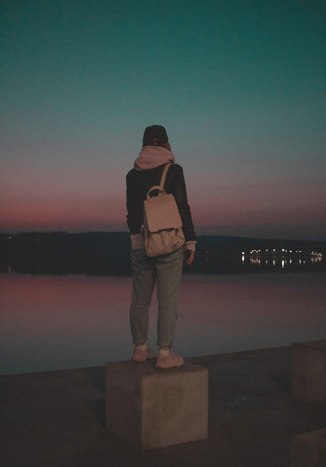 man in black jacket and brown pants standing on concrete dock during night time