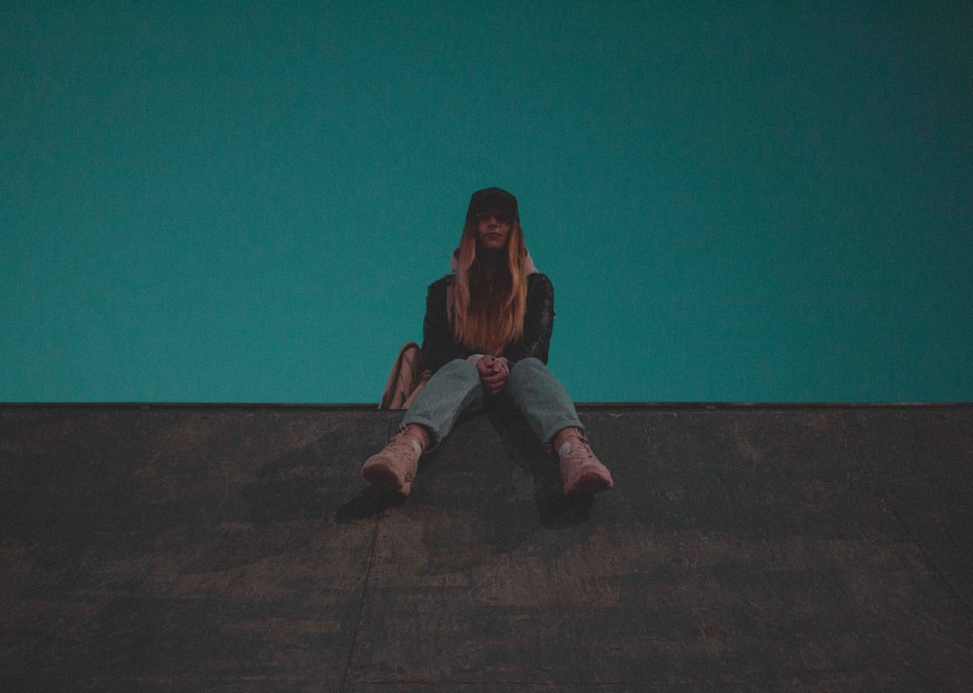 woman in brown jacket and blue denim jeans sitting on brown wooden floor