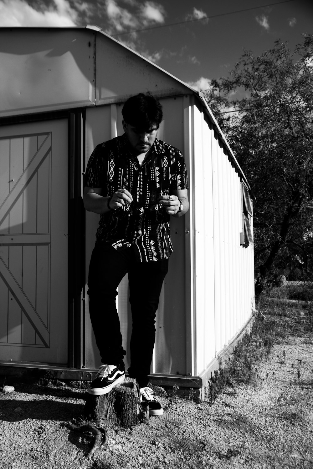 man in black and white plaid dress shirt and black pants standing beside white wooden door