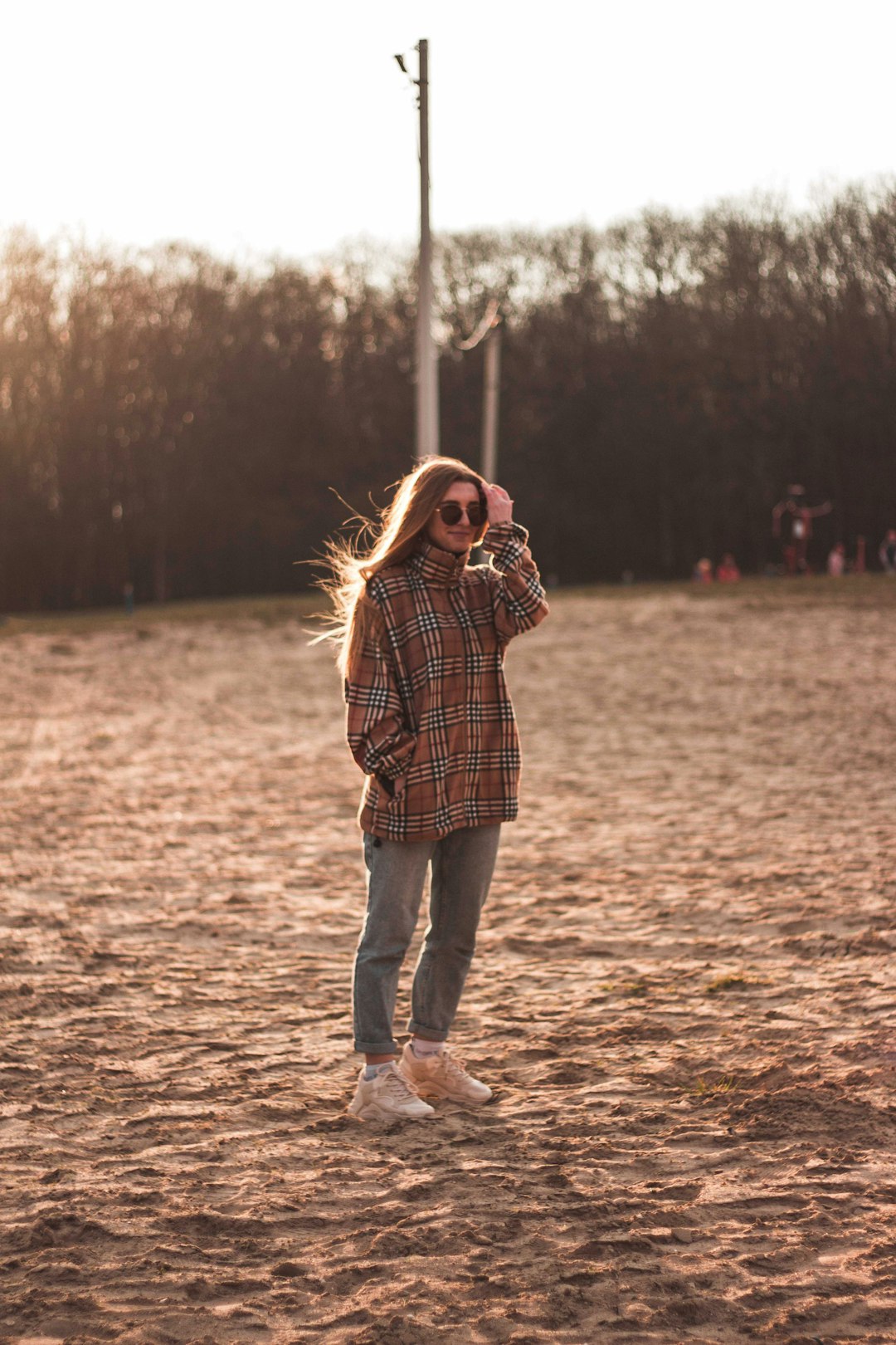 woman in brown and black plaid dress shirt and blue denim jeans standing on brown field