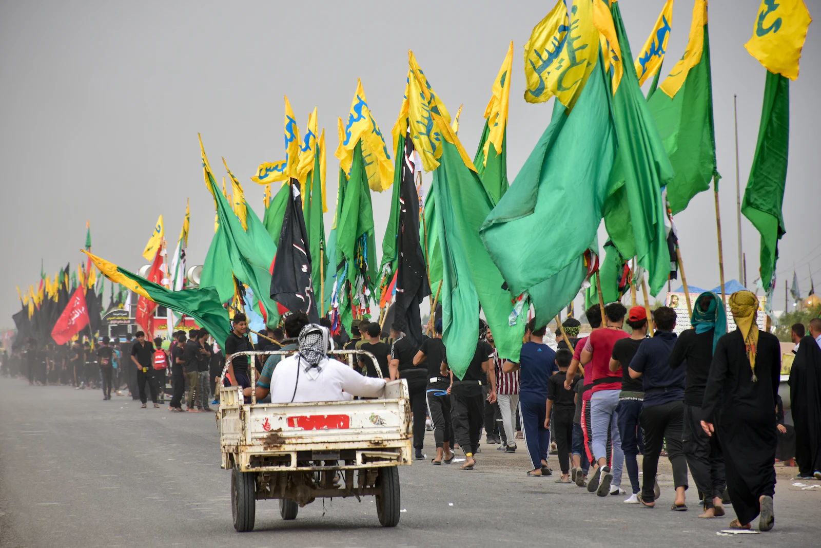 Pilgrims walking with green and gold banners on the road to Karbala