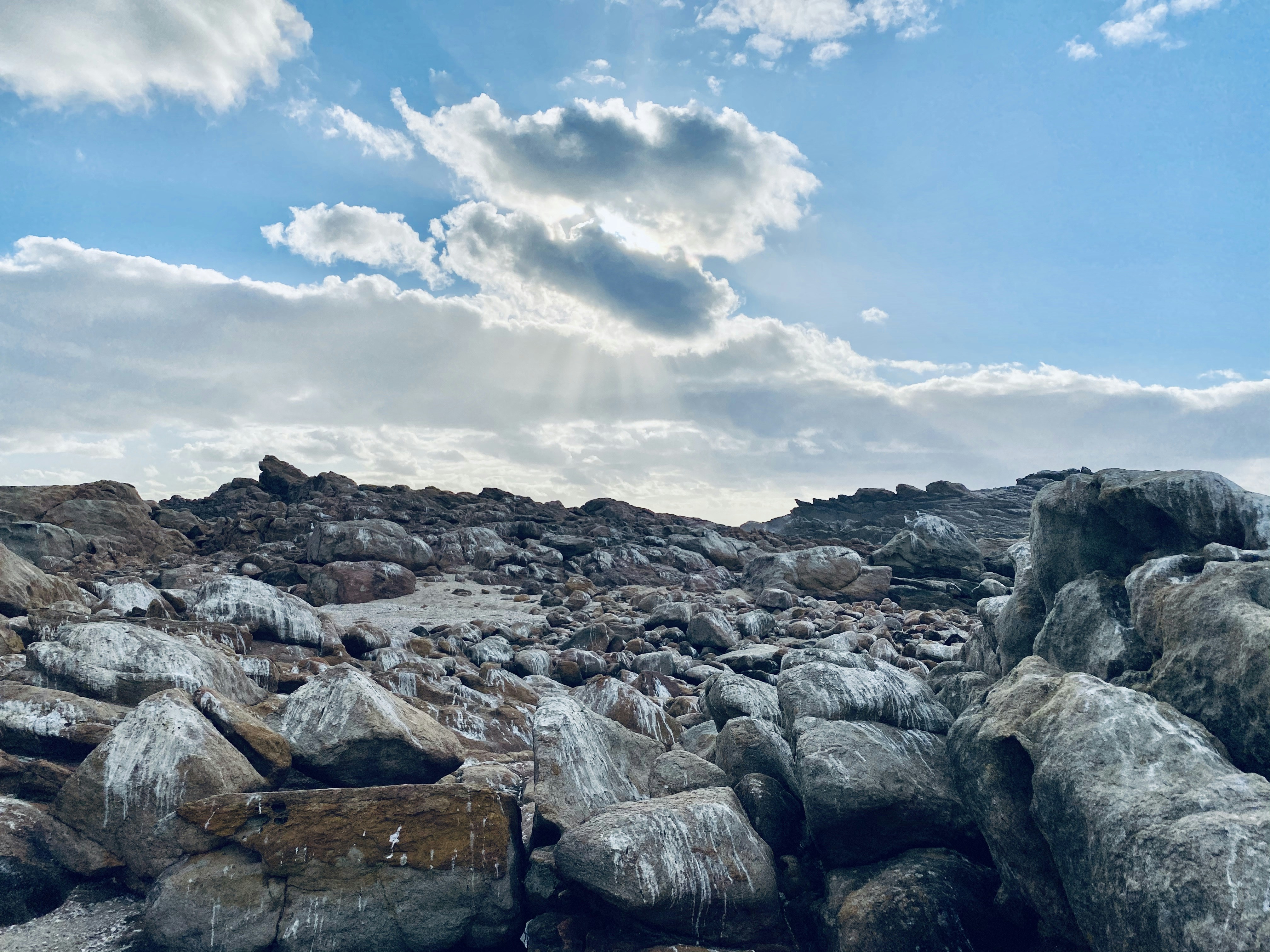 felsiges Ufer unter blauem Himmel und weißen Wolken tagsüber