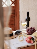A rustic wooden table set with a bottle of wine, cheese, and grapes.