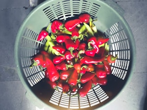 A vibrant close-up of fresh red chillies spilling from a rustic woven basket onto a wooden table.