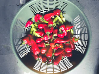 A rustic basket filled with vibrant dry red chilies resting on a wooden table in a sunlit spice market.