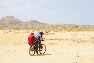 man in blue jacket riding bicycle on brown sand during daytime