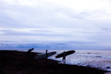 Sunset view of the beach with silhouettes of surfers carrying boards after class