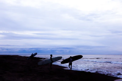 Sunset view of the beach with silhouettes of surfers carrying boards after class