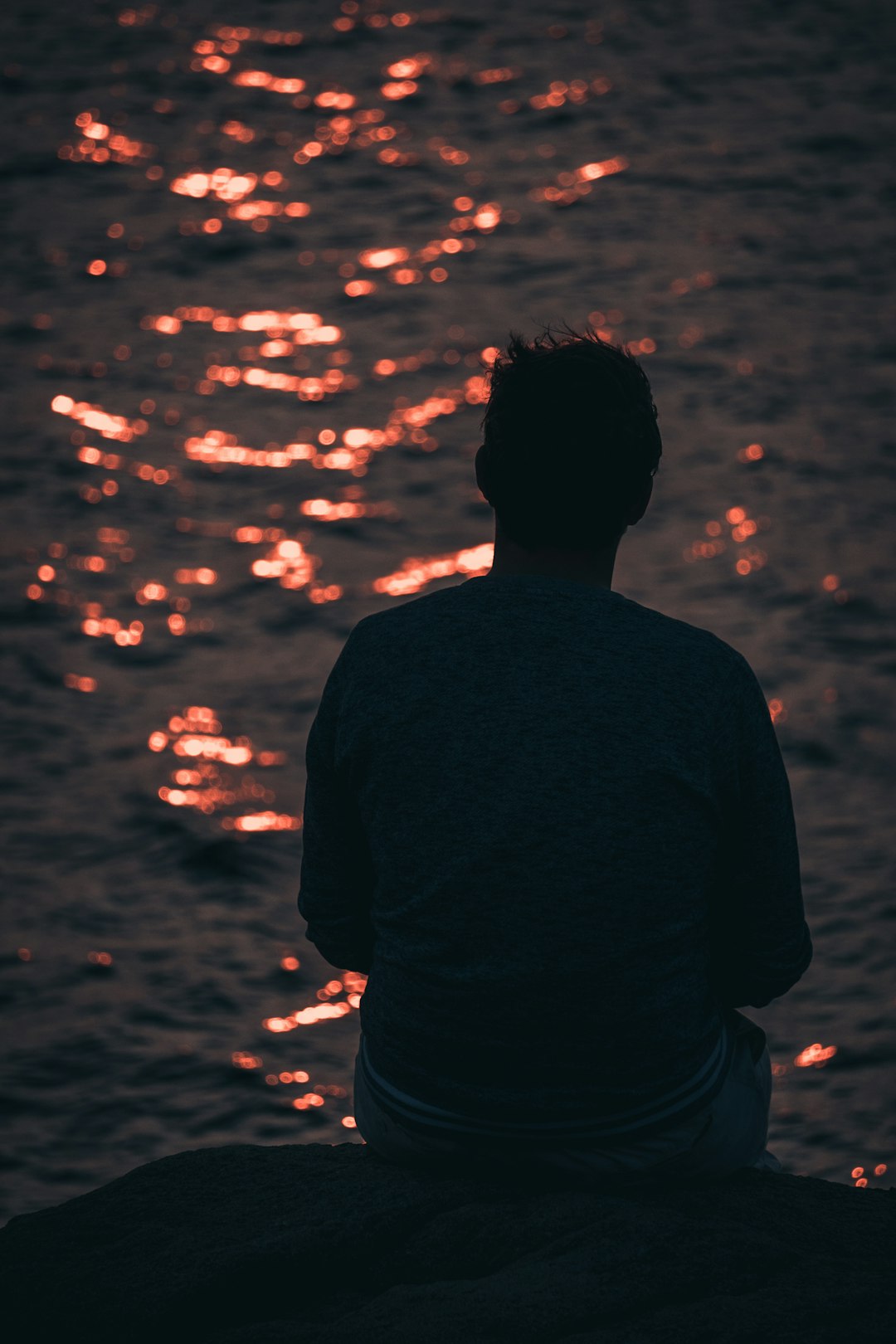 man in black shirt standing near body of water during sunset