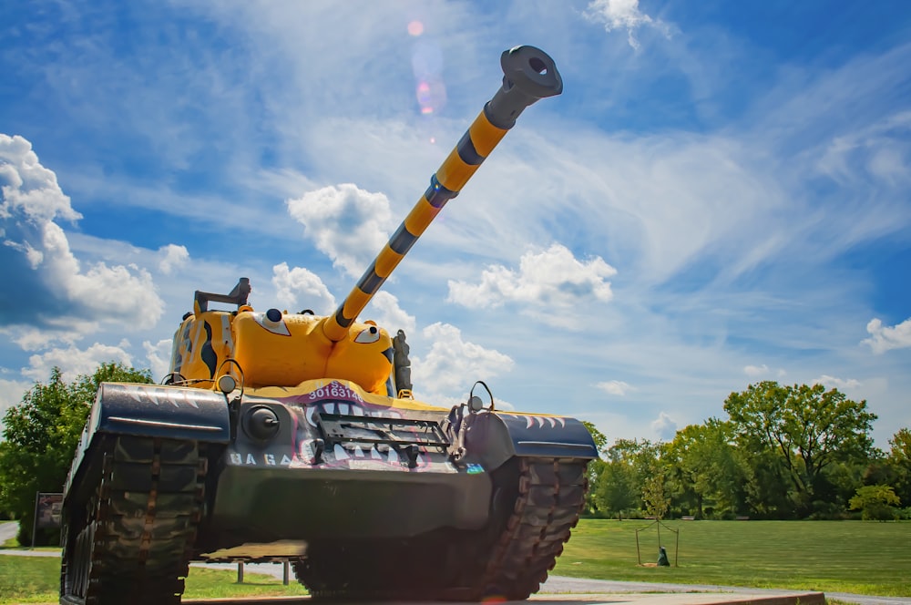 yellow and black battle tank on green grass field under white clouds and blue sky during