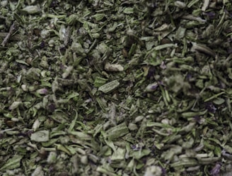 A close-up view of dried green herbs and leaves, showing a mix of finely chopped and crumbled pieces with a textured and natural appearance.
