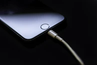 Lightning cable coiled neatly beside a smartphone on a dark surface with subtle blue lighting.