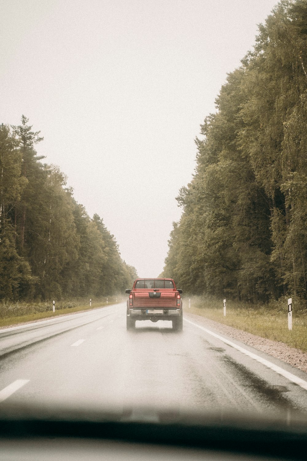 red suv on road between trees during daytime