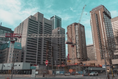 Several tall buildings are surrounded by construction activity, including cranes. The scene captures an urban environment with skyscrapers and ongoing construction work. A stop sign and street infrastructure are visible in the foreground.