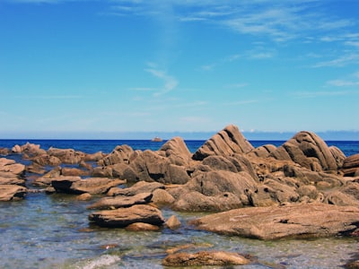 brown rocks on body of water under blue sky during daytime