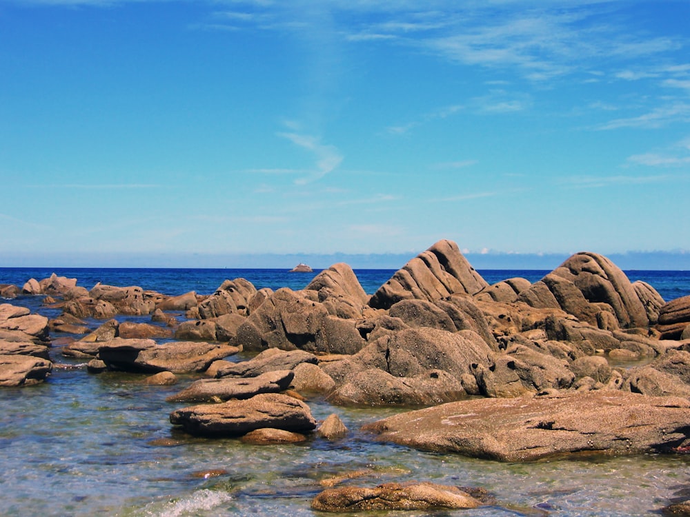 brown rocks on body of water under blue sky during daytime