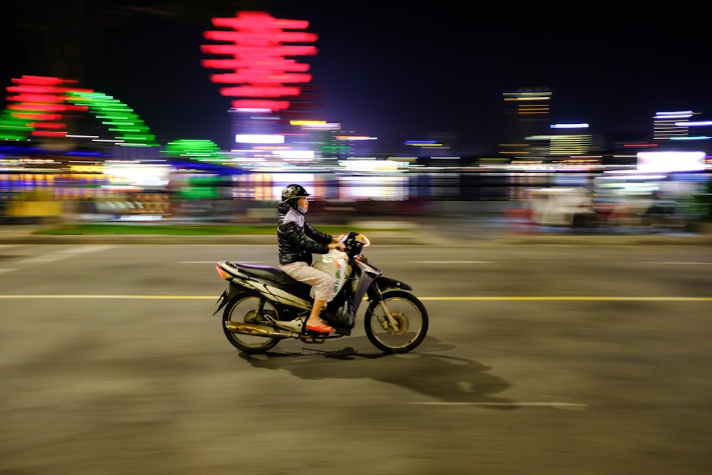 homem na jaqueta preta que monta a motocicleta na estrada durante a noite