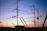 A variety of television antennas are silhouetted against a colorful sunset sky, with hues of orange, purple, and blue. The antennas are mounted on rooftops and connected by several cables, creating an intricate network of lines against the fading light.