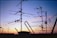A variety of television antennas are silhouetted against a colorful sunset sky, with hues of orange, purple, and blue. The antennas are mounted on rooftops and connected by several cables, creating an intricate network of lines against the fading light.