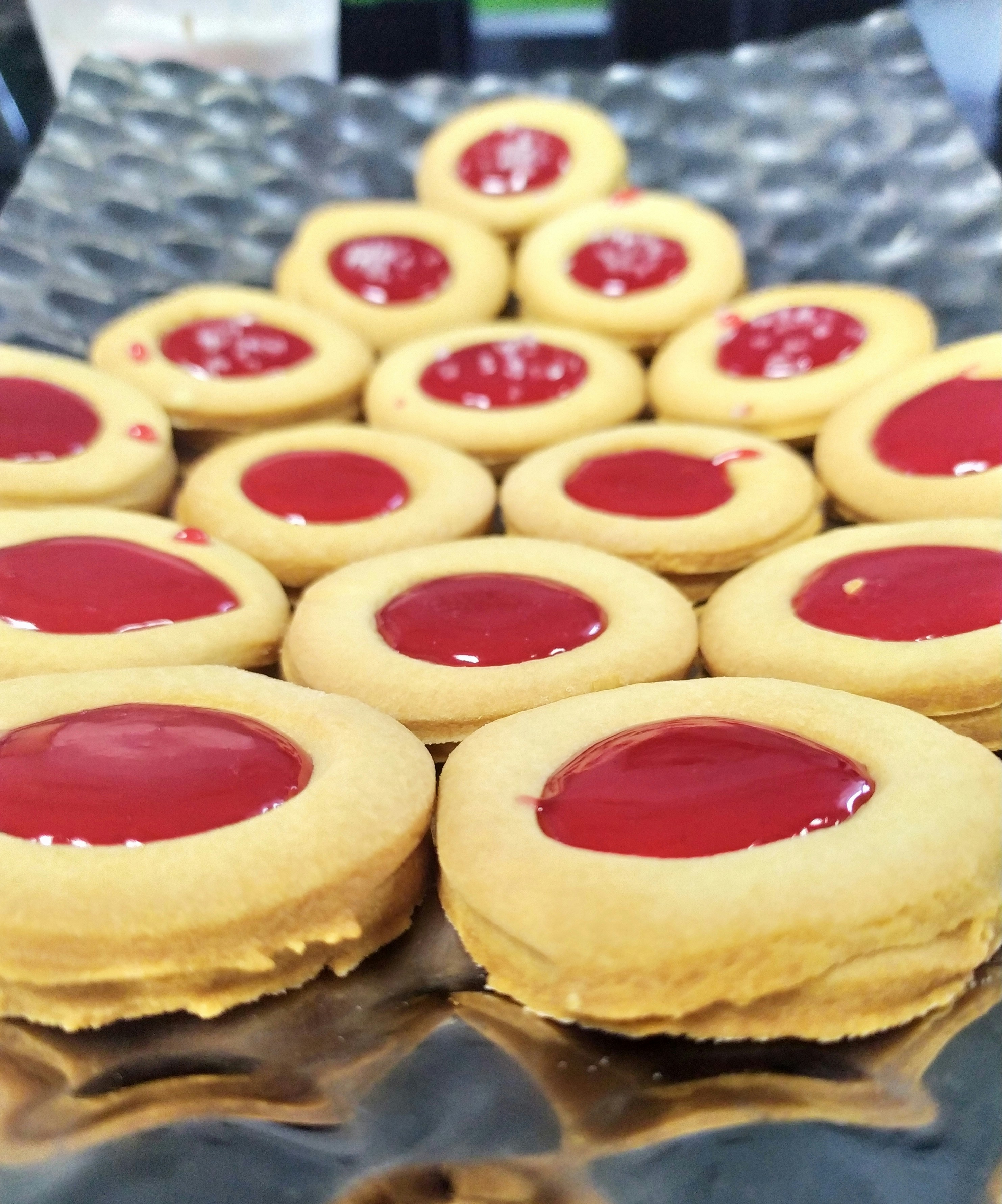 Delicate thumbprint cookies filled with bright red raspberry jam on a white ceramic plate, bright airy kitchen