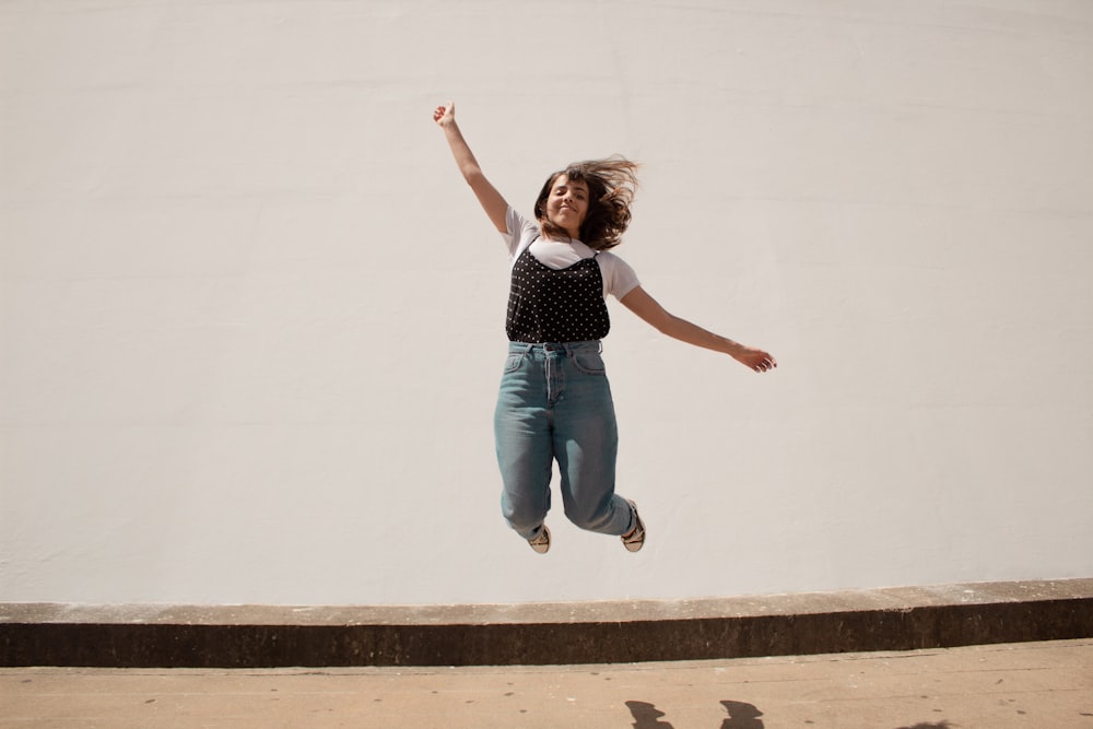 woman in white tank top and blue denim jeans jumping on brown wooden platform