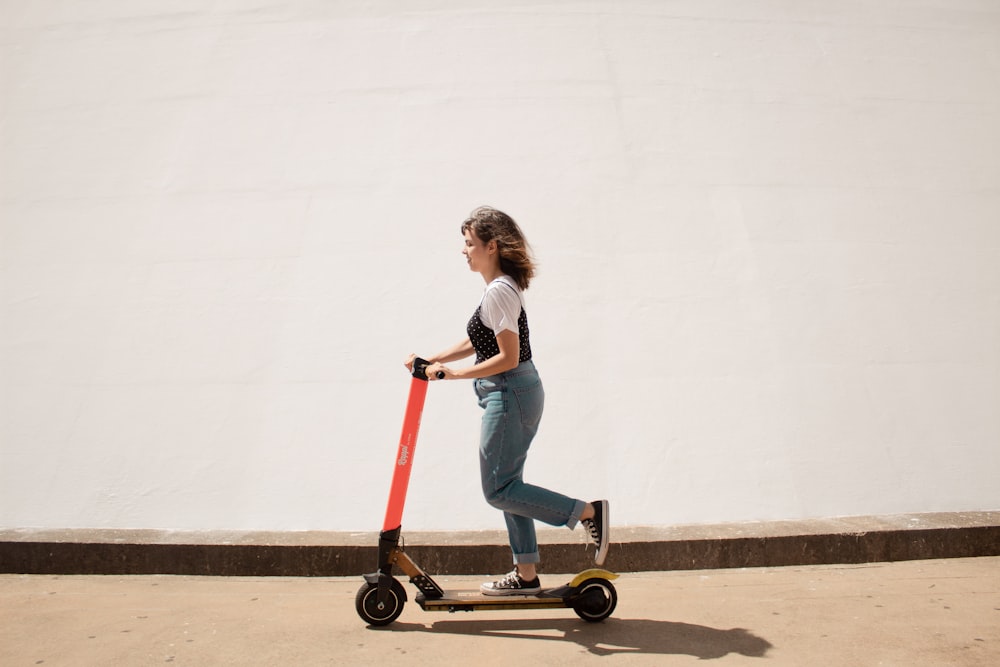 Mujer con camisa blanca y jeans de mezclilla azul montando patinete rojo y negro