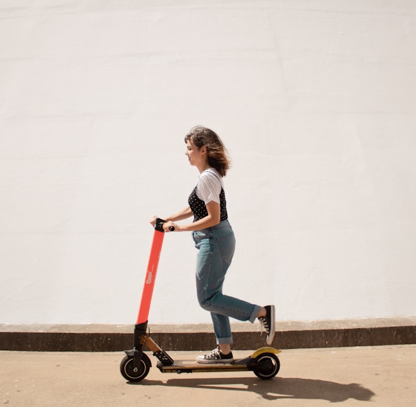woman in white shirt and blue denim jeans riding red and black kick scooter