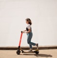 woman in white shirt and blue denim jeans riding red and black kick scooter