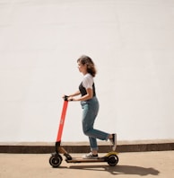 woman in white shirt and blue denim jeans riding red and black kick scooter