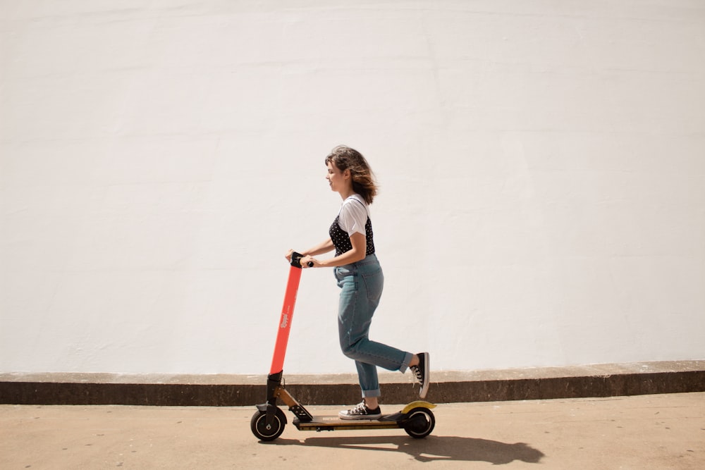 woman in white shirt and blue denim jeans riding red and black kick scooter
