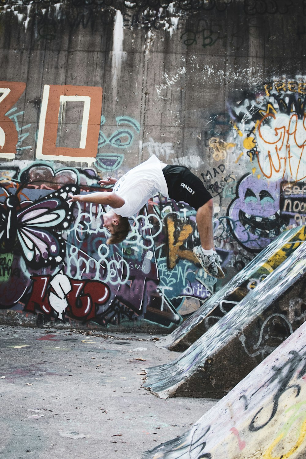 Hombre con camiseta blanca y pantalones cortos negros montando monopatín