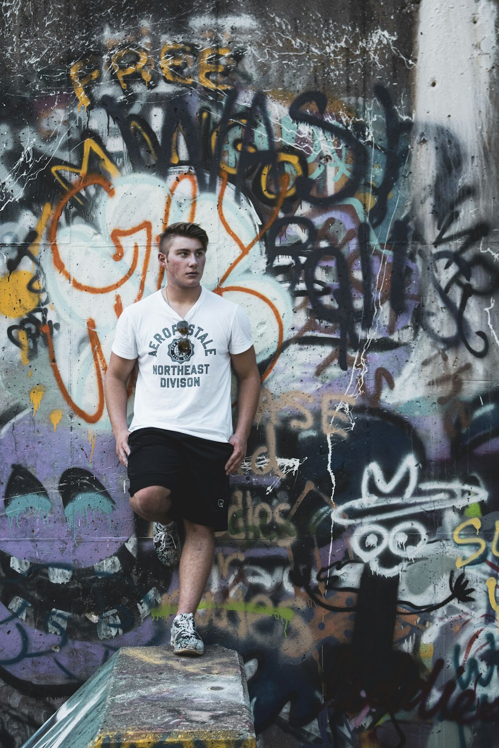 man in white crew neck t-shirt and black shorts standing beside graffiti wall